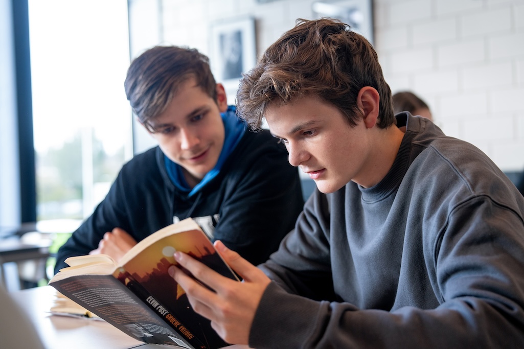 Jongen leest een boek en klasgenoot kijkt over schouder.