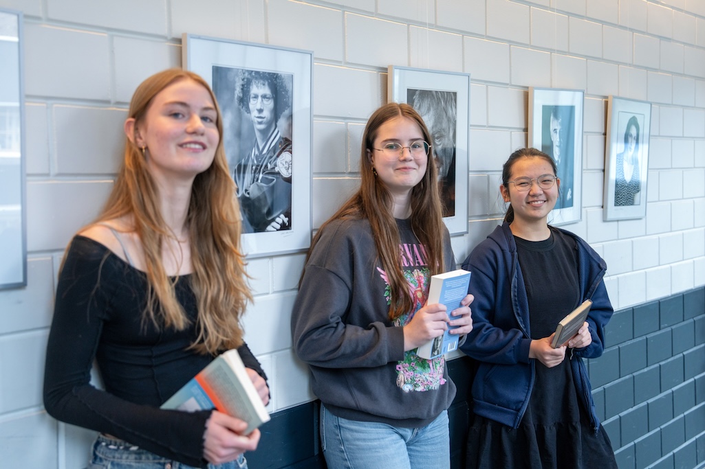 Drie scholieren tegen een muur geleund met elk een boek in de handen.
