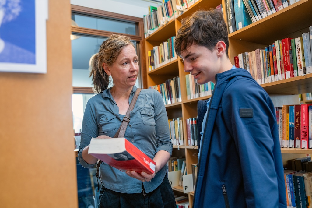 Lerares laat leerling boek zien in de schoolbibliotheek.