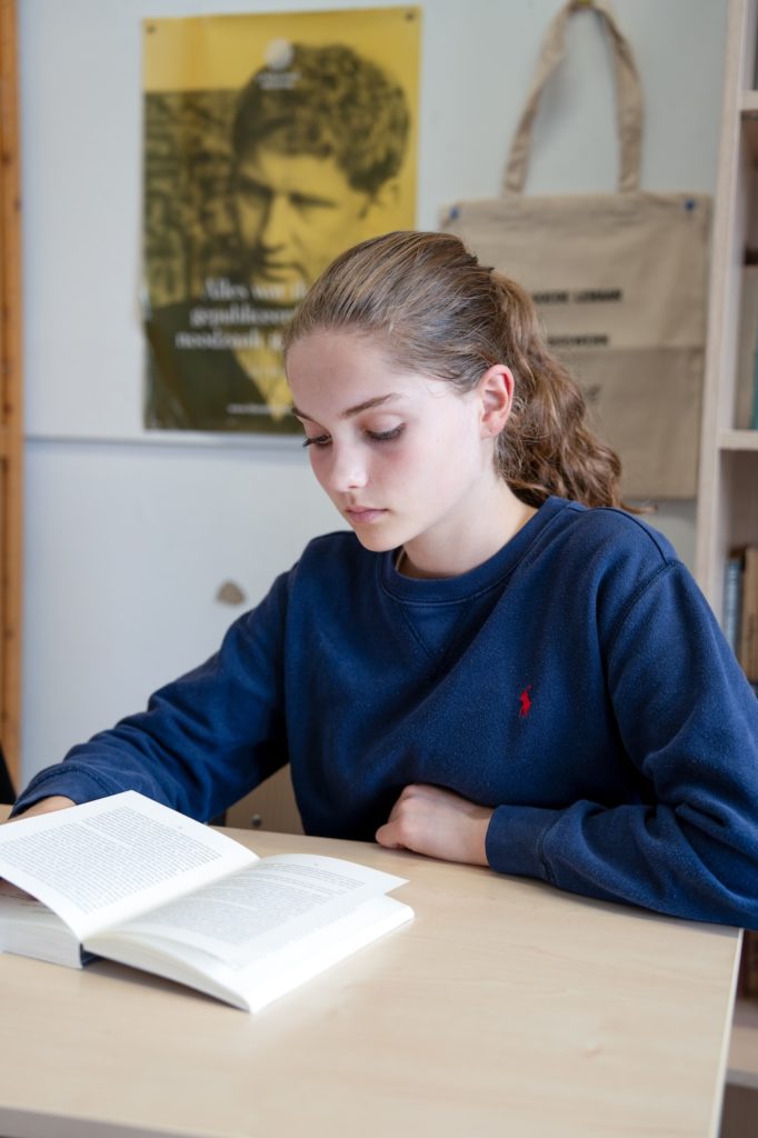 Leerlinge met paardenstaart leest een boek dat op haar bureau ligt.