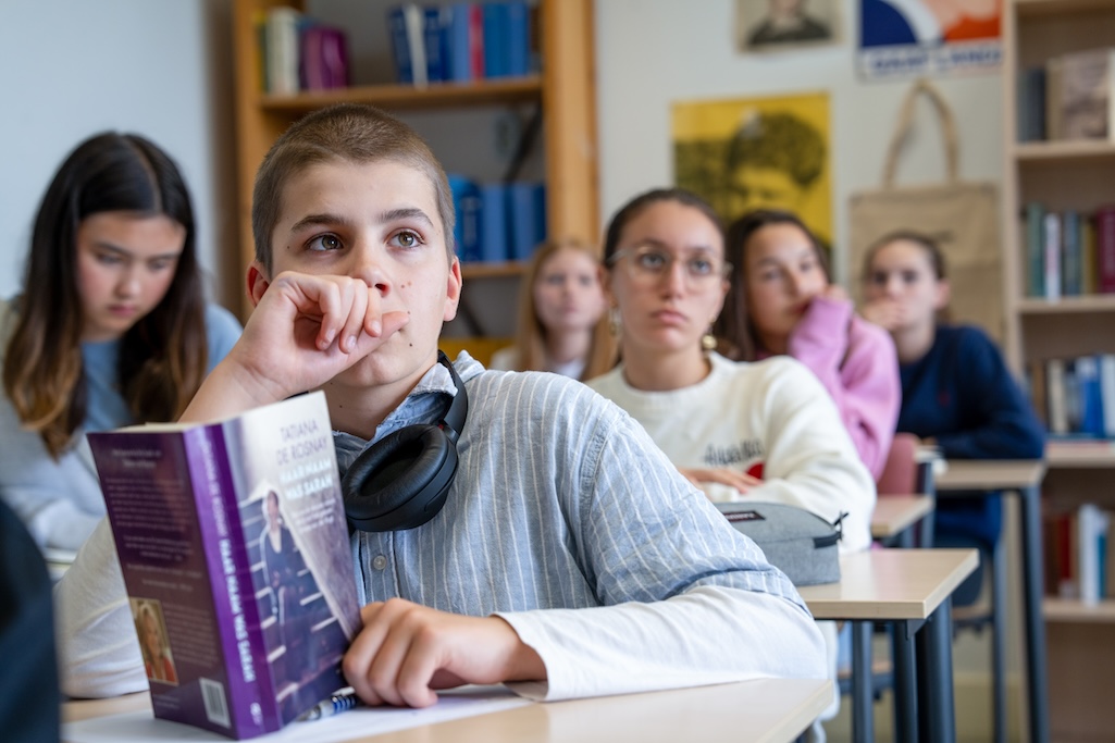 Leerling kijkt met boek in hand op van tafel