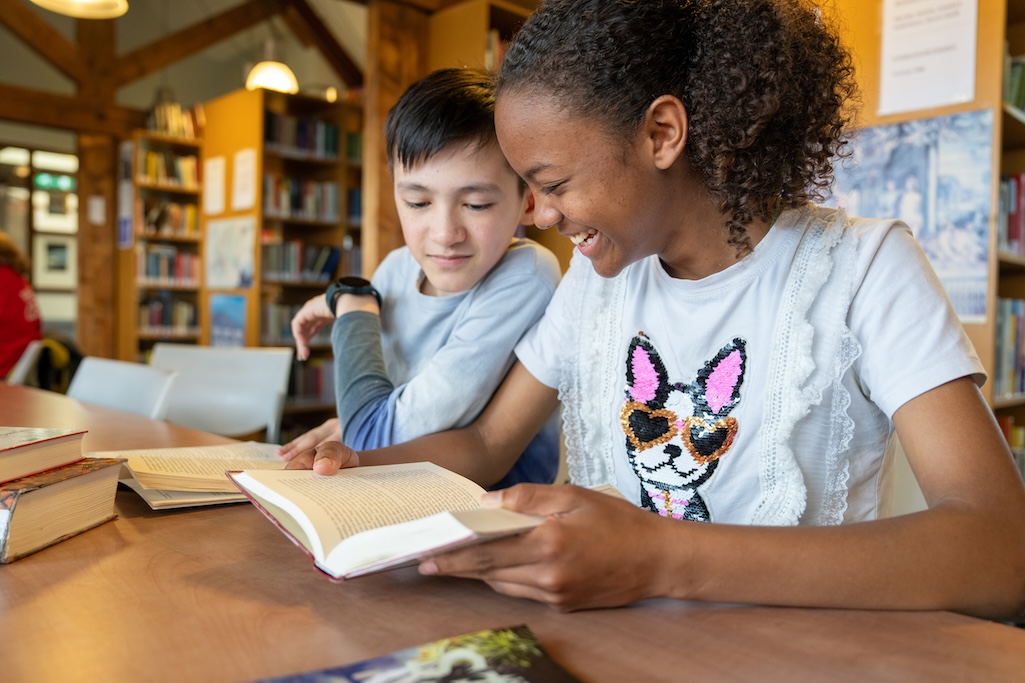 Leerlingen lezen boek aan tafel.