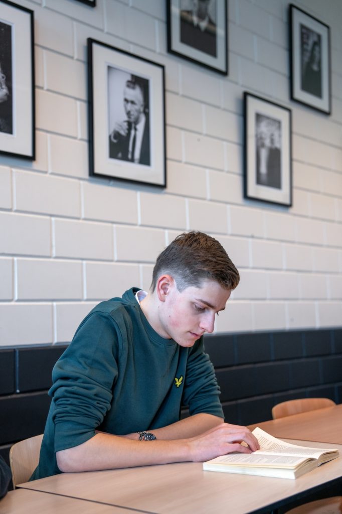 Jongen met blauwgroene trui die aan een schooltafel in een kalslokaal een boek leest