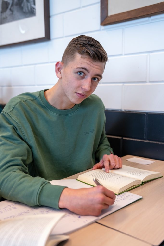 Jongen met groenblauwe trui die in de klas aan een schrijfopdracht werkt