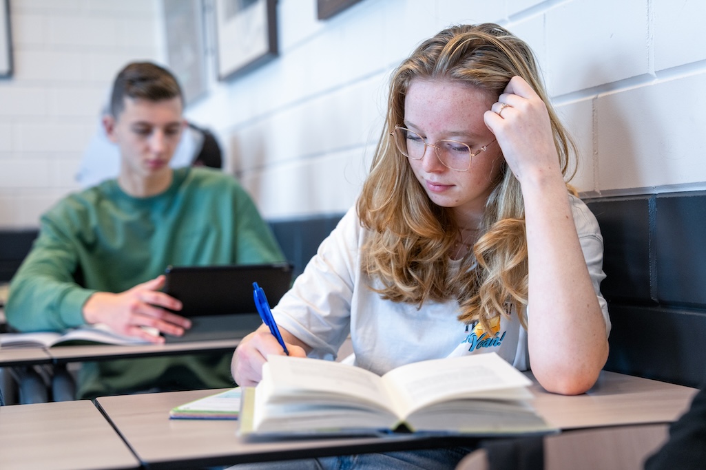 Leerling leest een boek in klaslokaal, aan een tafel.