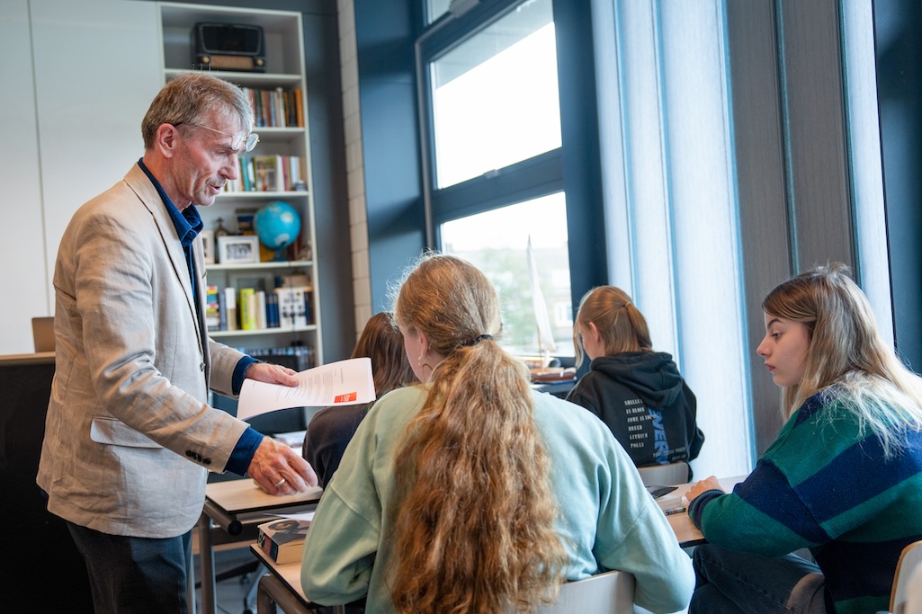 Docent deelt teksten uit bij leerling aan tafel